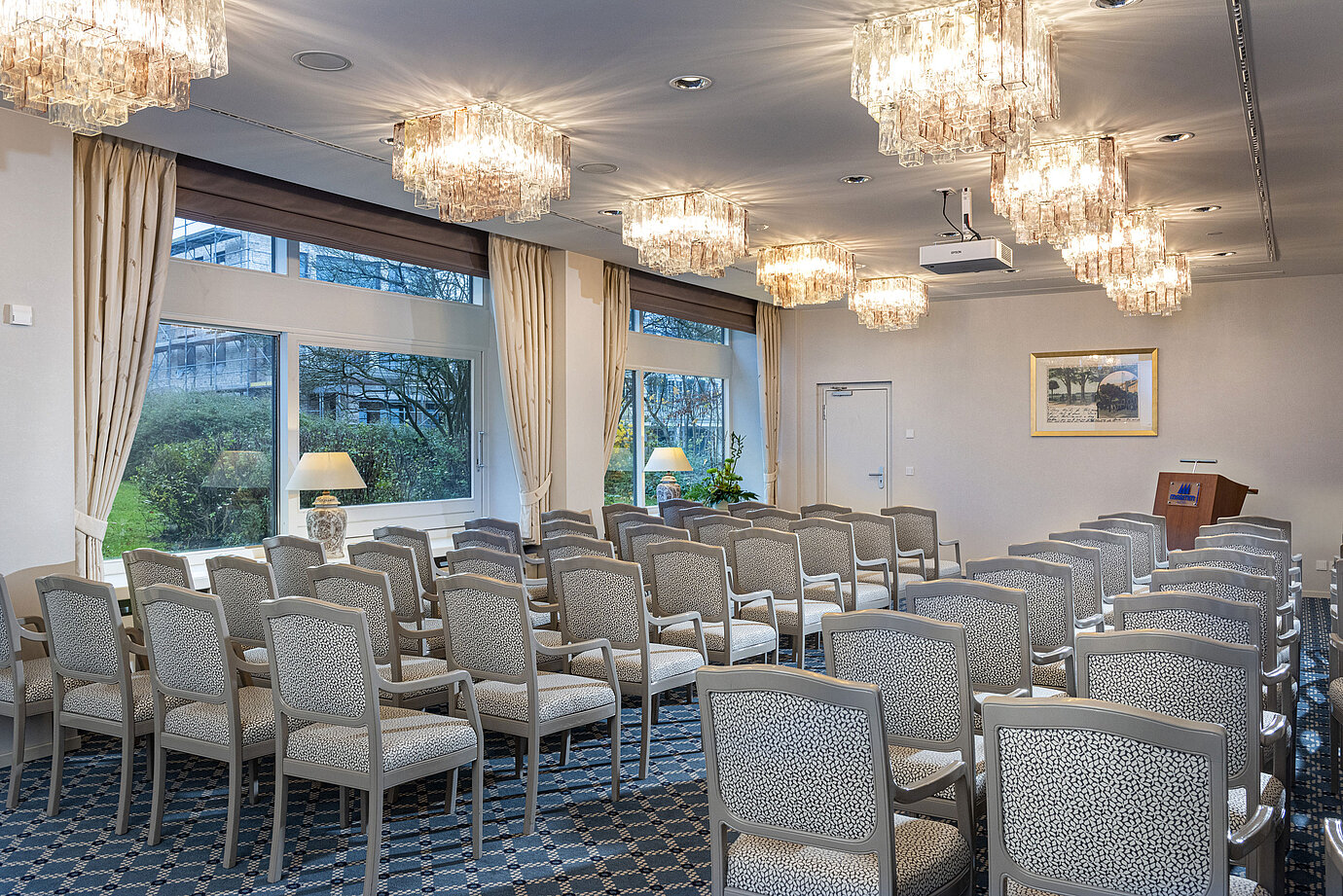 Salón Helsinki en el Maritim Hotel Kiel, sala de conferencias con hileras de sillas, lámparas de araña y grandes ventanales con vistas a la vegetación.