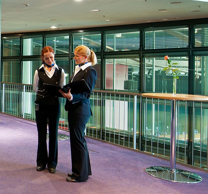 Foyer in Maritim Hotel Dresden with two staff members in uniform, standing tables, and a fruit station.