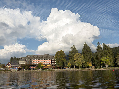 Exterior view of Maritim Hotel Titisee with trees and lakeside under blue sky and clouds