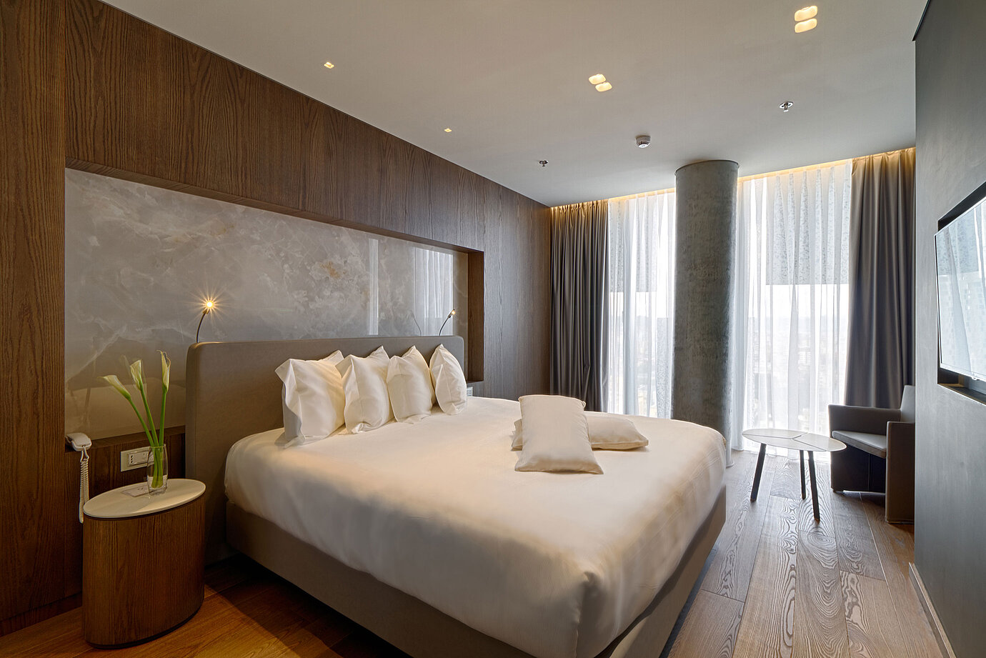 Chambre calme avec grand lit, mur en pierre naturelle et rideaux doux au Maritim Hotel Plaza Tirana