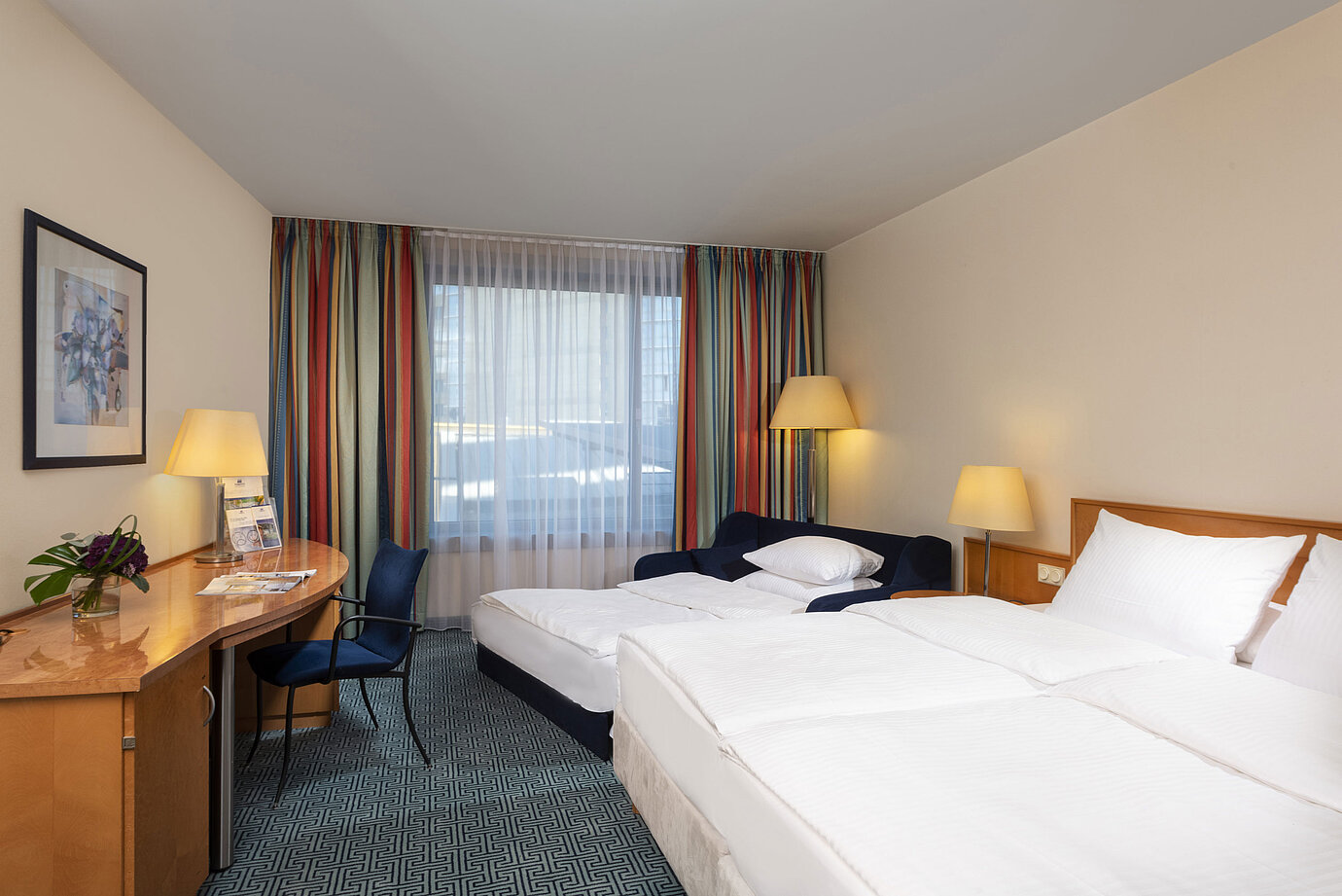 Camera familiare Classic del Maritim Hotel Frankfurt con letto matrimoniale, divano letto, scrivania e tende colorate.