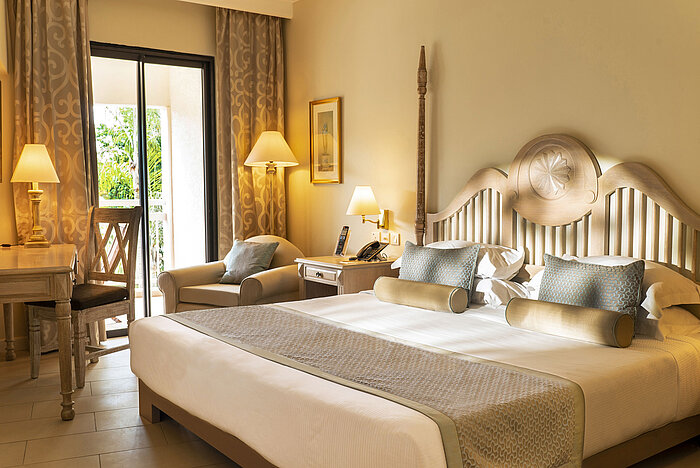 Suite con cama con dosel, zona de estar y baño abierto en el Maritim Hotel