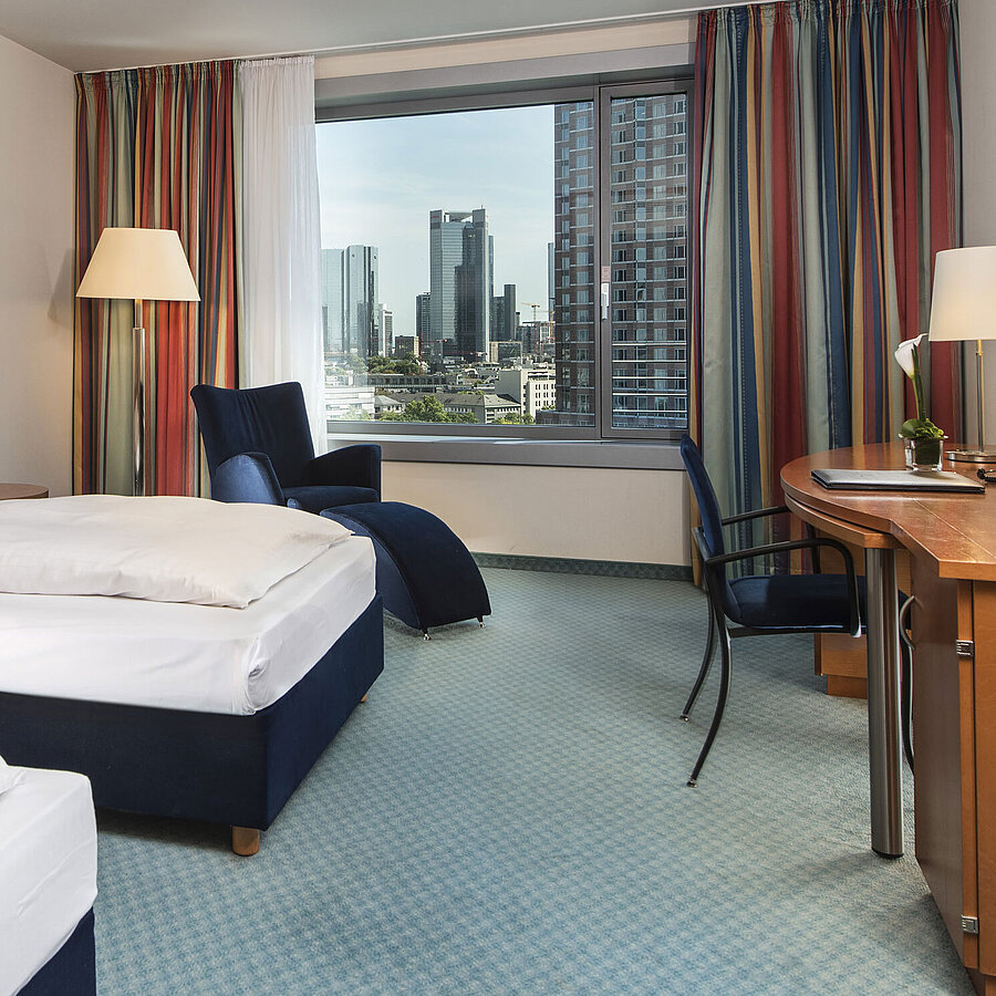 Camera Comfort Camera comfort al Maritim Hotel Frankfurt con due letti singoli, scrivania, area salotto e vista sulla skyline.