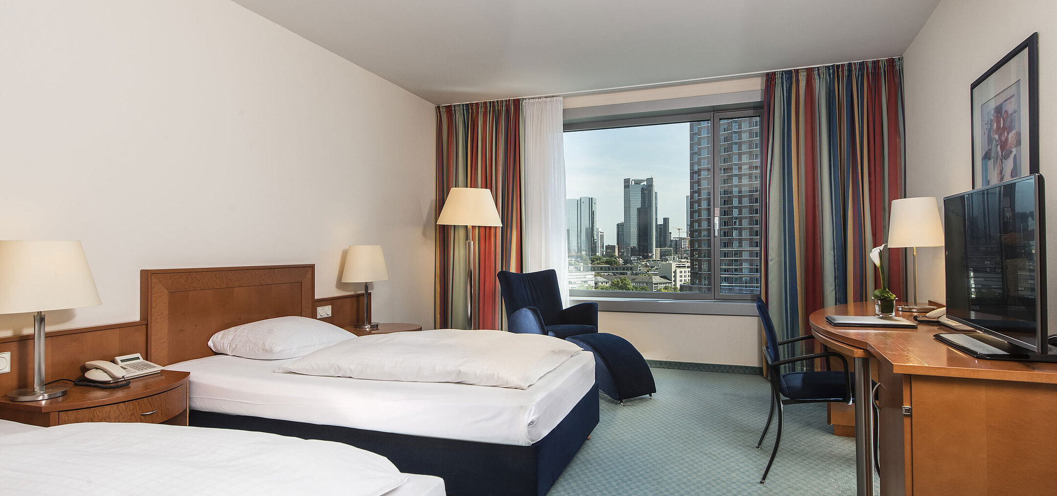 Chambre confort à l'hôtel Maritim Frankfurt avec deux lits simples, bureau, coin salon et vue sur la skyline.
