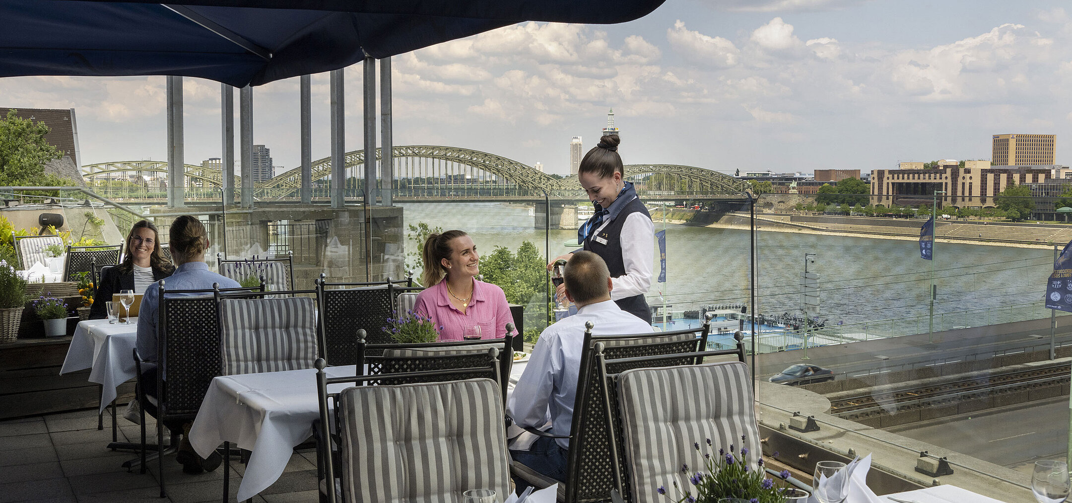Los huéspedes disfrutan del servicio en la terraza del Hotel Maritim Colonia con vistas al río Rin y al puente Hohenzollern.