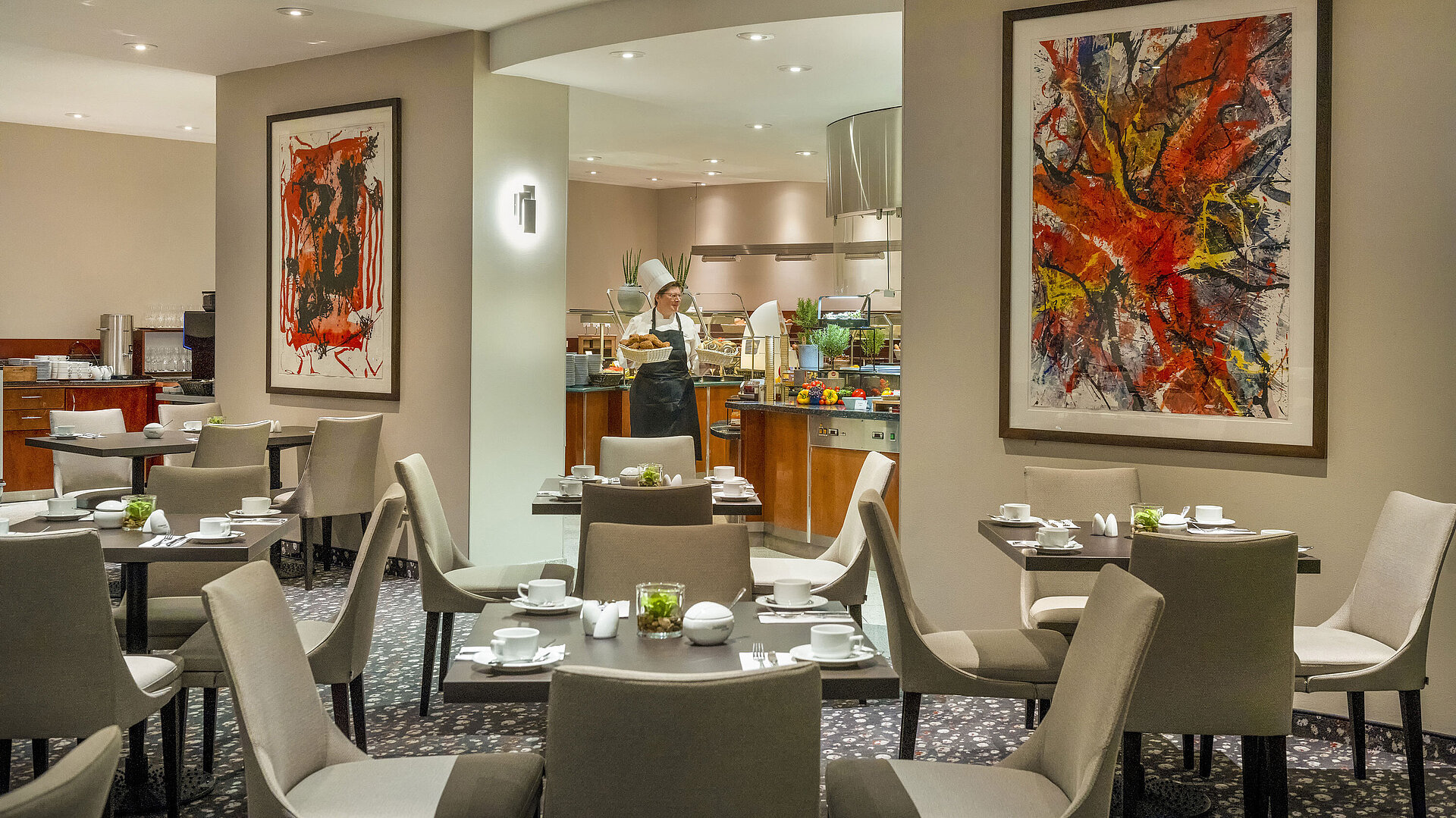 Restaurant du Maritim proArte Hotel Berlin avec de l'art moderne sur les murs, des tables nappées et un cuisinier au buffet.