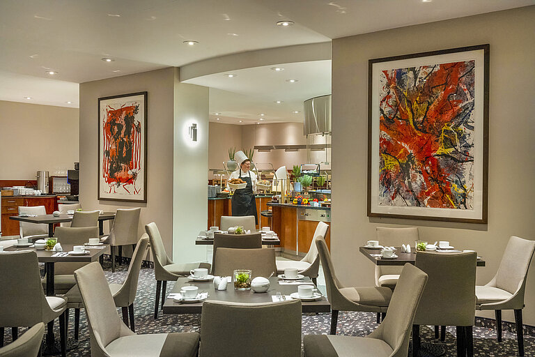 Restaurant du Maritim proArte Hotel Berlin avec de l'art moderne sur les murs, des tables nappées et un cuisinier au buffet.