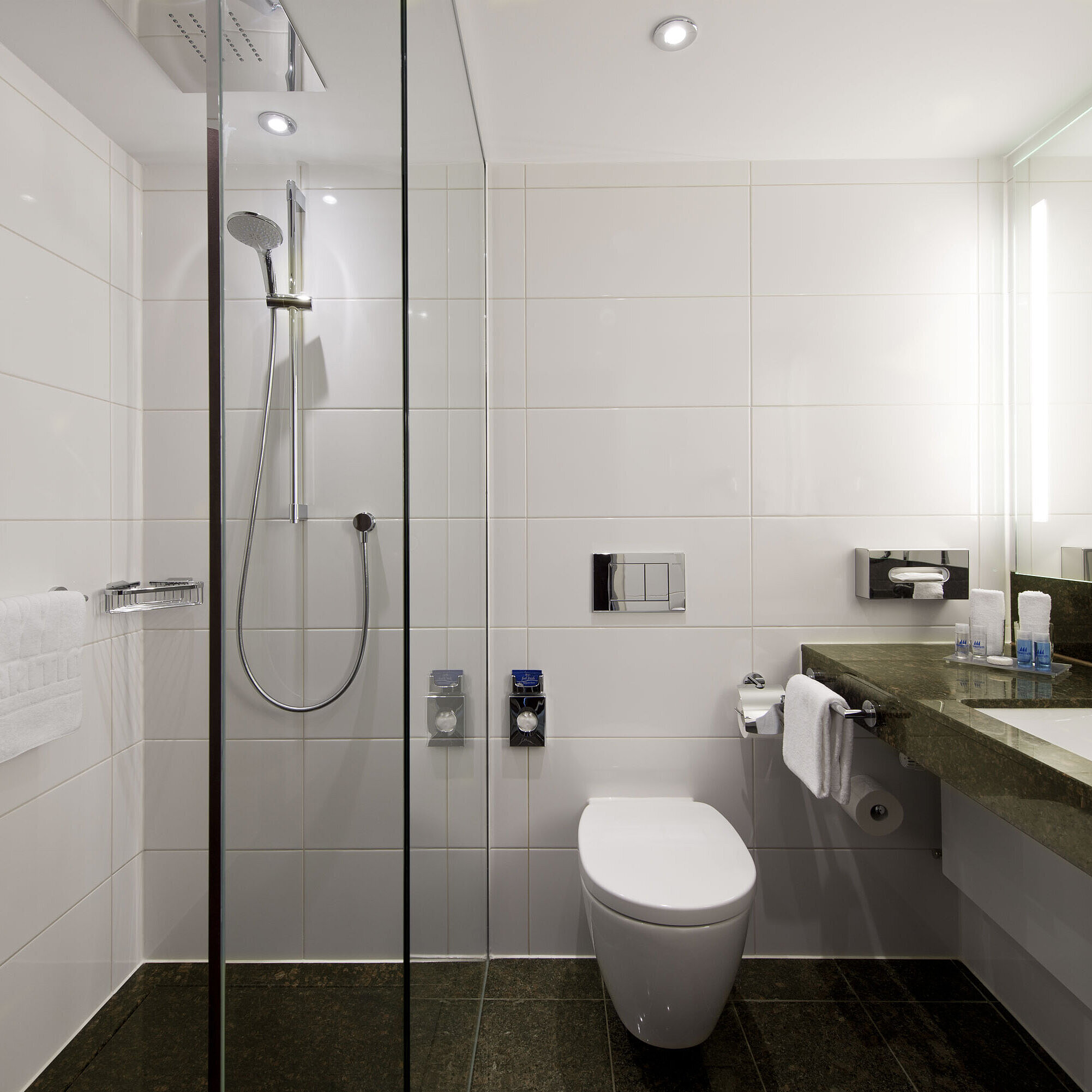 Salle de bain avec douche Salle de bain du Maritim Hotel Darmstadt avec douche à effet pluie spacieuse, design moderne et surface en granit foncé.