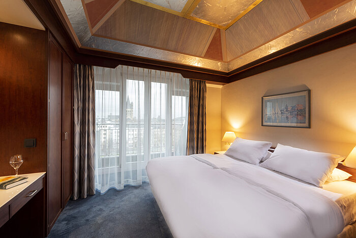 Junior Suite con un grande letto, scrivania, soffitto elegante e vista panoramica dalle grandi finestre.