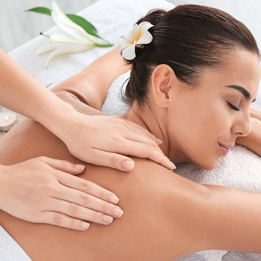 Woman relaxing during soothing back massage in spa with flower in hair
