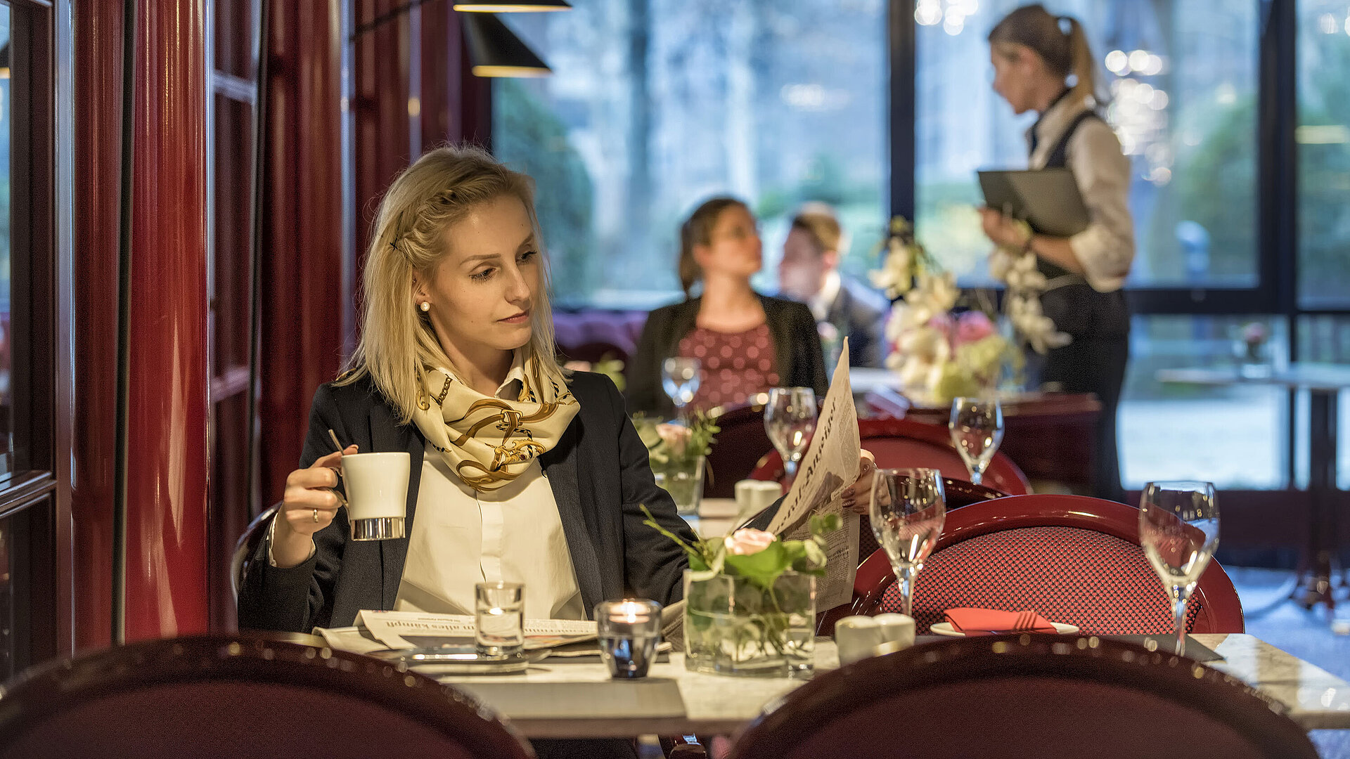 Woman enjoying coffee at the "Brasserie" café in Maritim Hotel Bonn with red decor and a relaxed atmosphere.