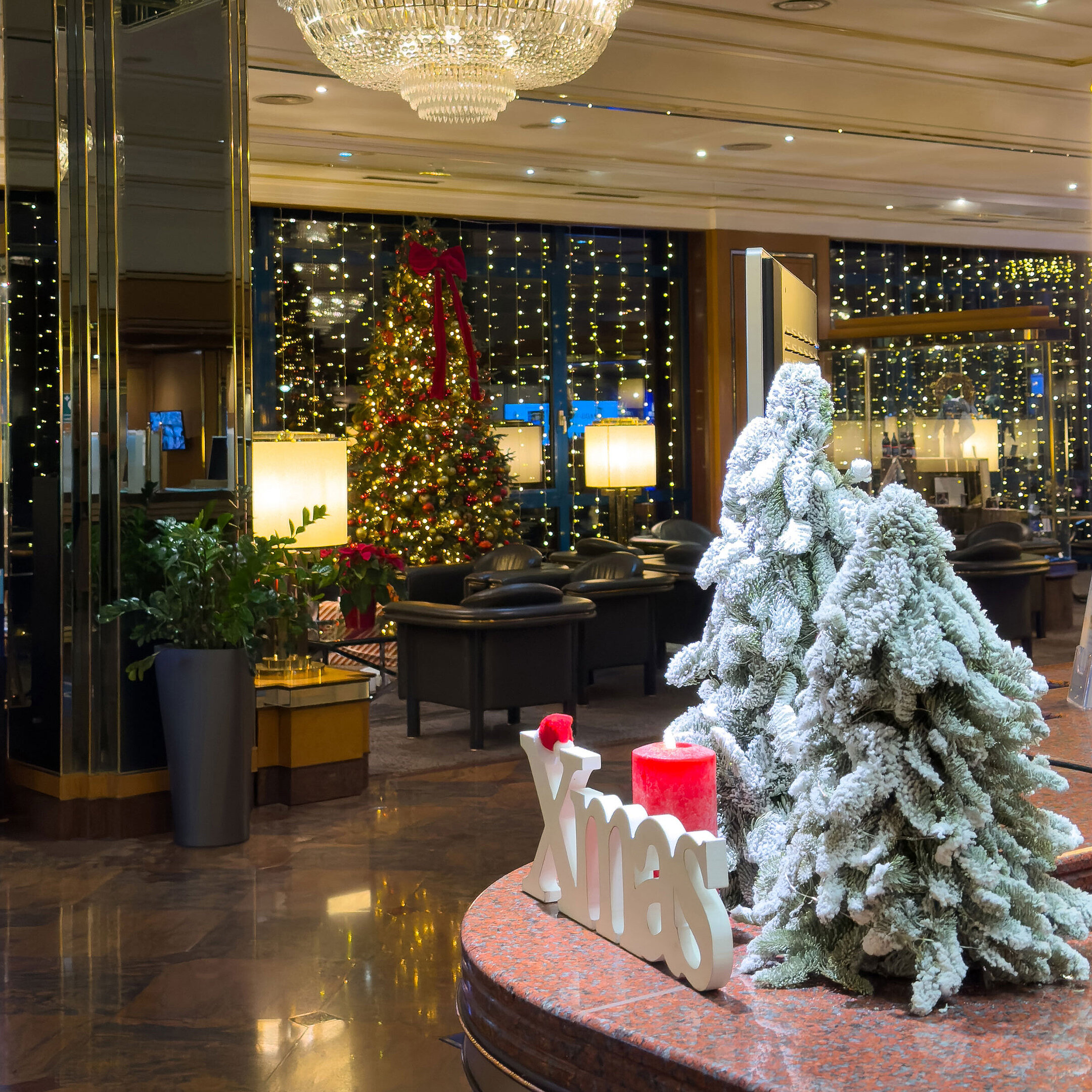 Festively decorated hotel lobby with Christmas trees, chandelier and a warm winter atmosphere.