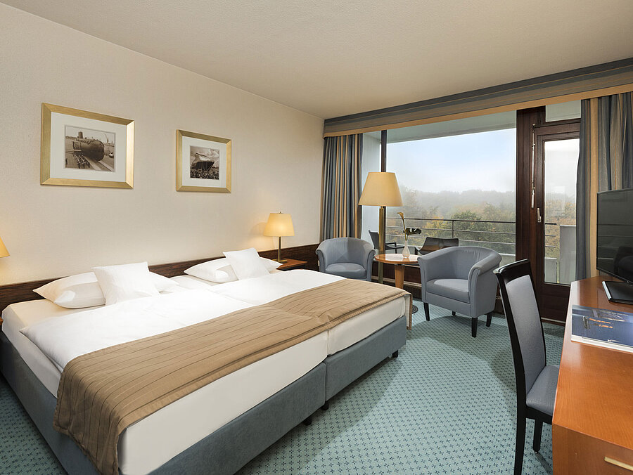 Classic room at the Maritim Hotel Kiel with large double bed, seating area, desk and balcony with a view of the countryside.
