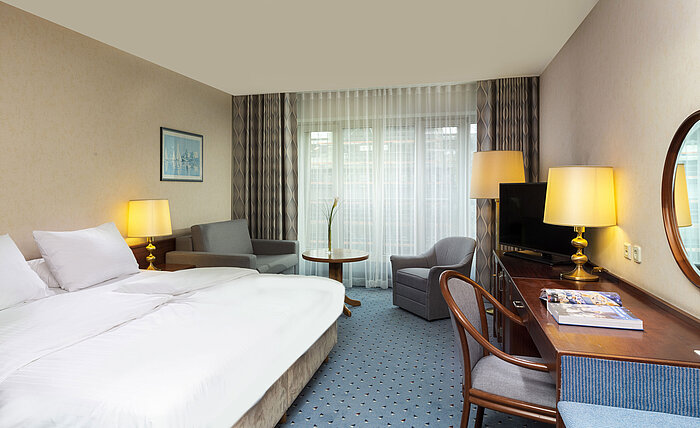 Camera Comfort al Maritim Hotel Colonia con letto matrimoniale, scrivania, divano e interni moderni con ampie finestre.