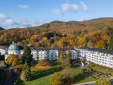 Vista exterior del Maritim Hotel Bad Wildungen rodeado de parque, árboles y un paisaje forestal otoñal.