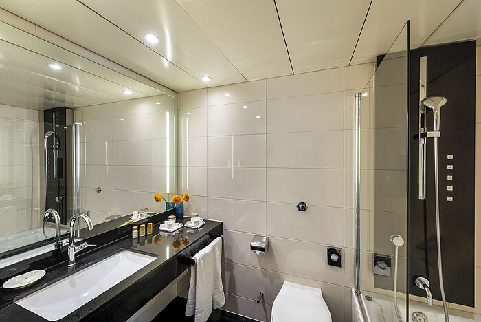 Bagno moderno con vasca da bagno, grande specchio, rubinetteria elegante e comfort di alta qualità presso il Maritim Hotel Ulm.