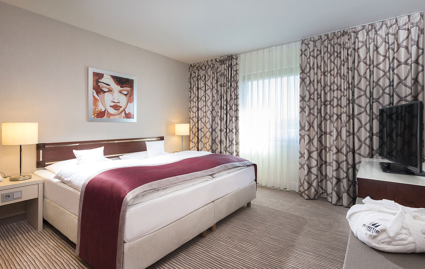 Ampia suite presso il Maritim Hotel Bonn con letto matrimoniale accogliente, arredamento moderno e copriletto rosso vino.