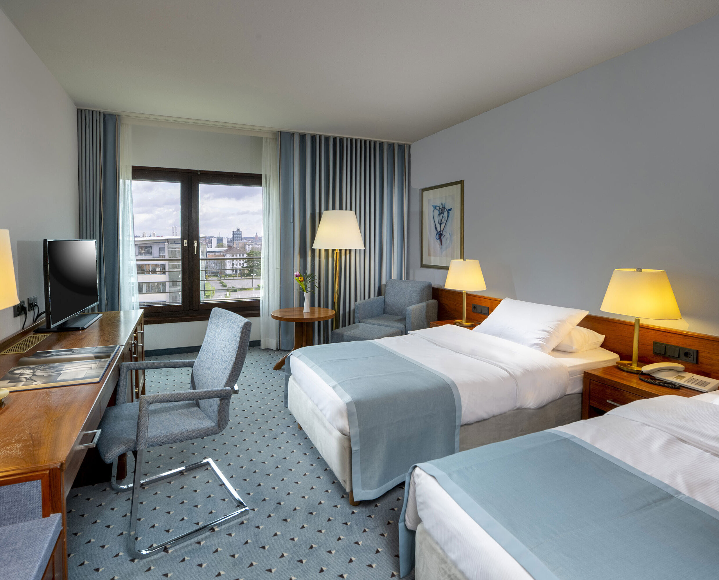 Chambre Comfort twin Chambre twin confort à l'hôtel Maritim Darmstadt avec bureau, deux lits simples et fenêtre panoramique avec vue sur la ville.