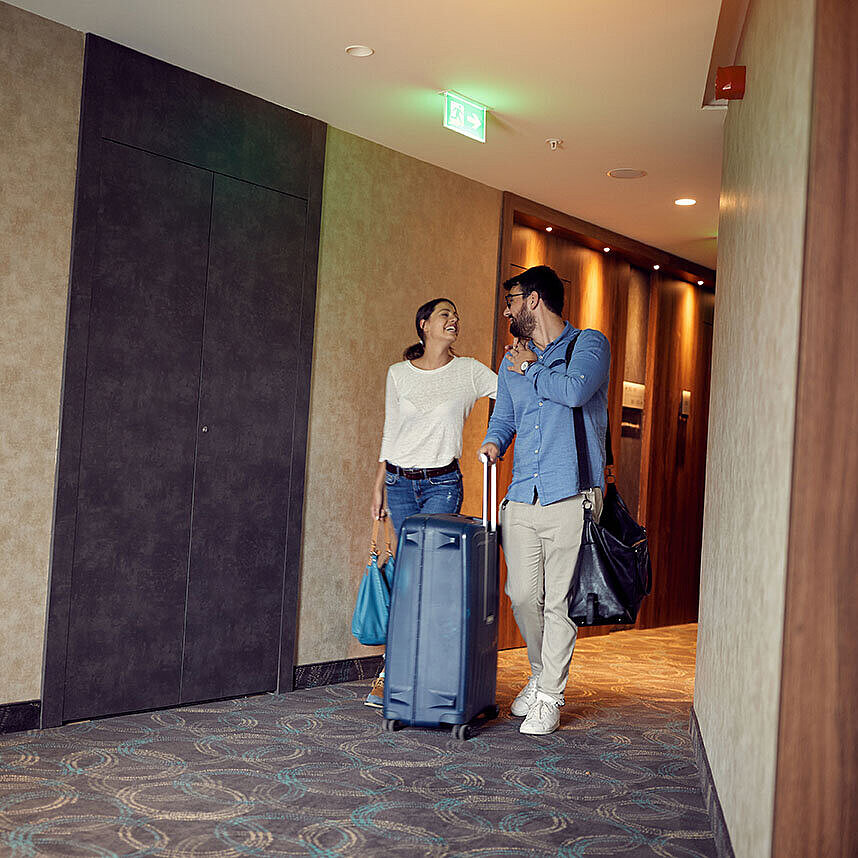 Couple with luggage in hotel corridor looking forward to their stay