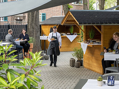 Un serveur sert des plats lors d'un événement sur la terrasse du Maritim Hotel Darmstadt avec des cabanes en bois