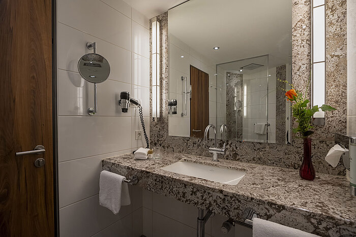 Salle de bain moderne à l'hôtel Maritim Bad Homburg avec lavabo en granit, miroir et éclairage élégant.