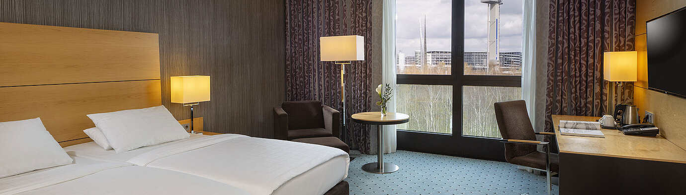 Chambre classique au Maritim Hotel Düsseldorf avec lit double, bureau et fenêtre panoramique avec vue sur les environs.