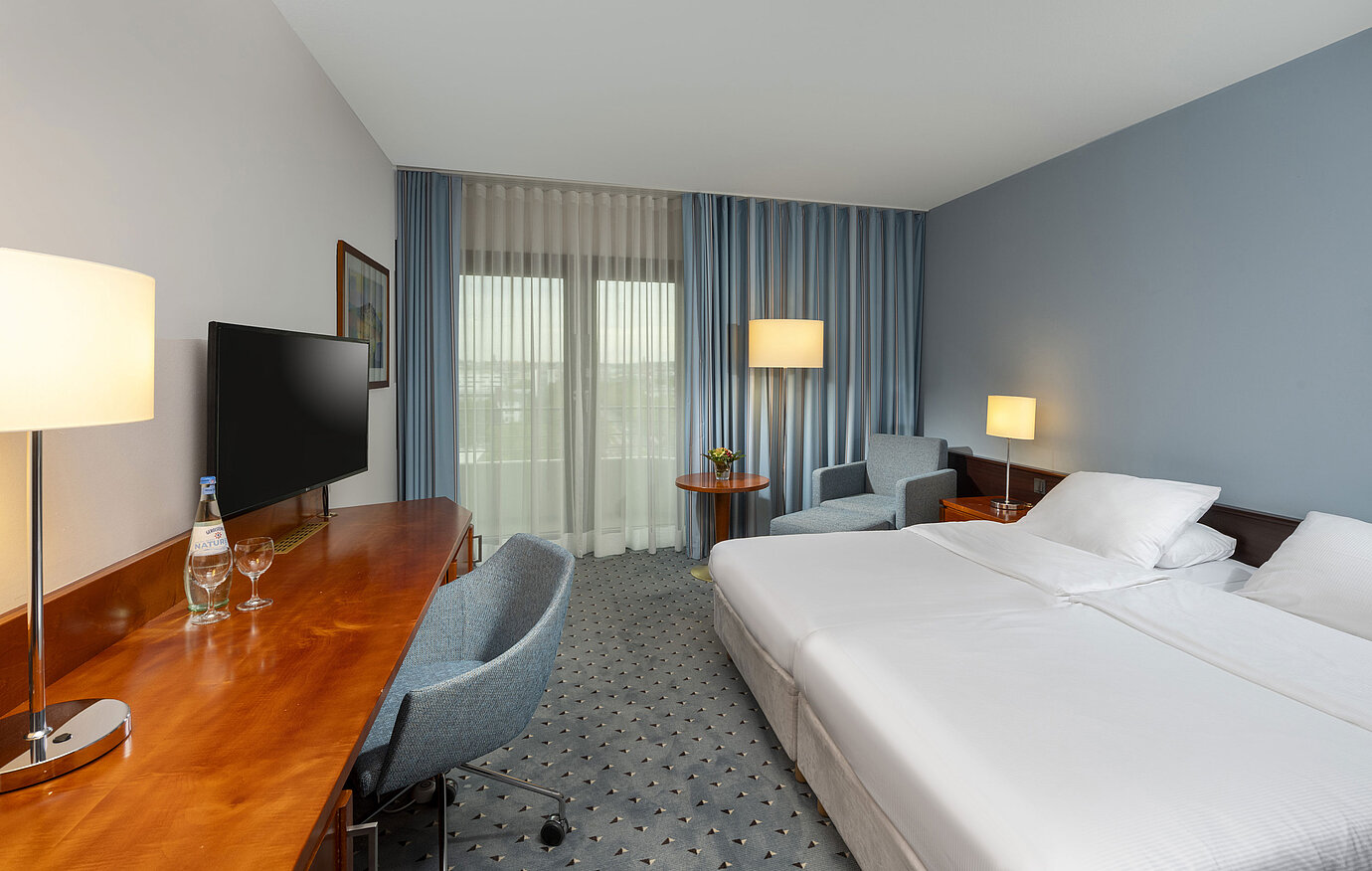 Classic double room at Maritim Hotel Darmstadt with desk, flat-screen TV, seating area, and large windows with curtains.