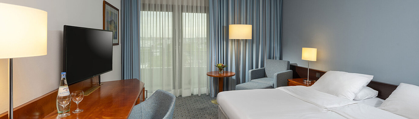 Camera doppia classica al Maritim Hotel Darmstadt con scrivania, TV a schermo piatto,area salotto e grandi finestre con tende