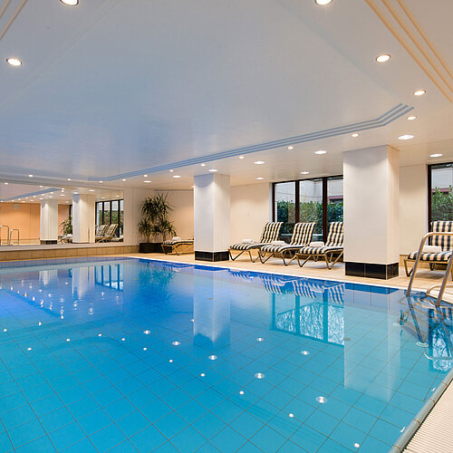 Piscine intérieure moderne au Maritim Hotel Fulda avec transats, grandes fenêtres et ambiance relaxante.