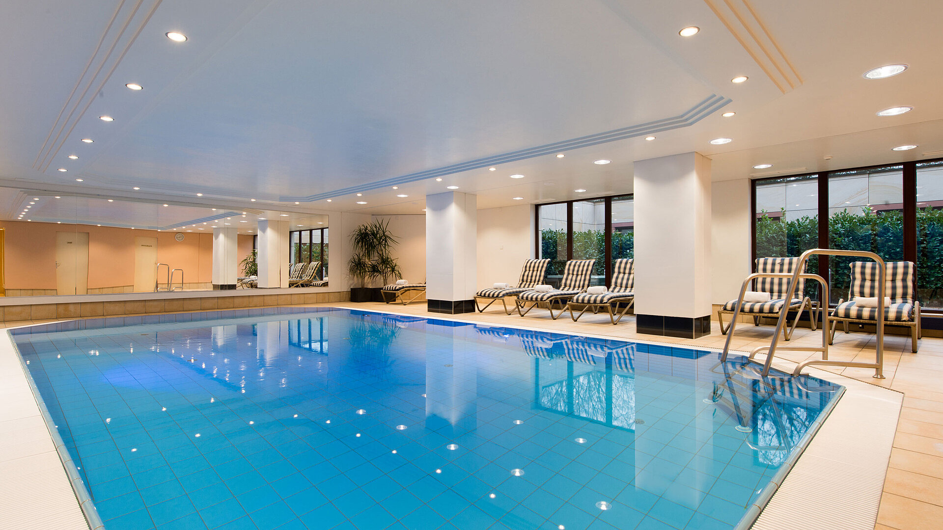 Piscina Piscina cubierta moderna en Maritim Hotel Fulda con tumbonas, grandes ventanales y ambiente relajante.