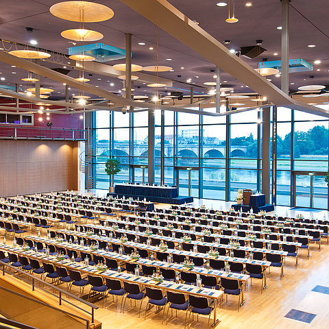 Grande salle de conférence de l'hôtel Maritim de Dresde avec des rangées de chaises bleues et vue sur l'Elbe.
