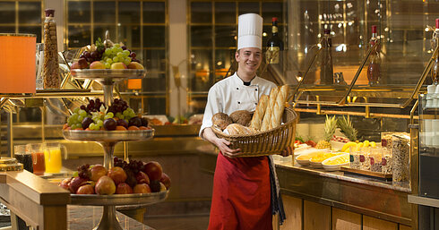 Baker with basket of bread at breakfast buffet at Maritim Hotel Stuttgart, surrounded by fresh fruit