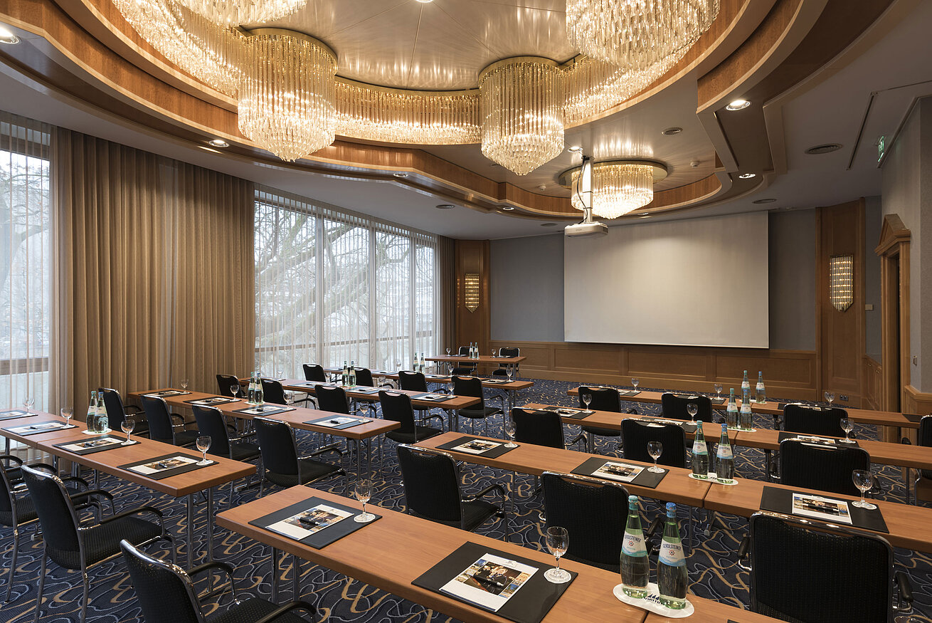 Salle de conférence élégante avec rangées de sièges, lustres et écran au Maritim Hotel Ulm.