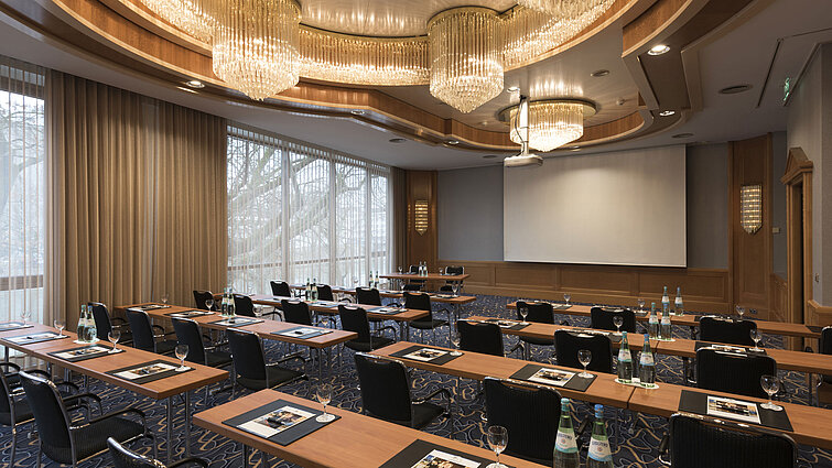 Sala de conferencias elegante con sillas en fila, lámparas y pantalla en el Maritim Hotel Ulm.