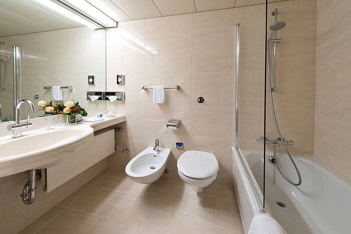 Bagno elegante con vasca, doccia, lavandino e specchio presso il Maritim Hotel Hannover.