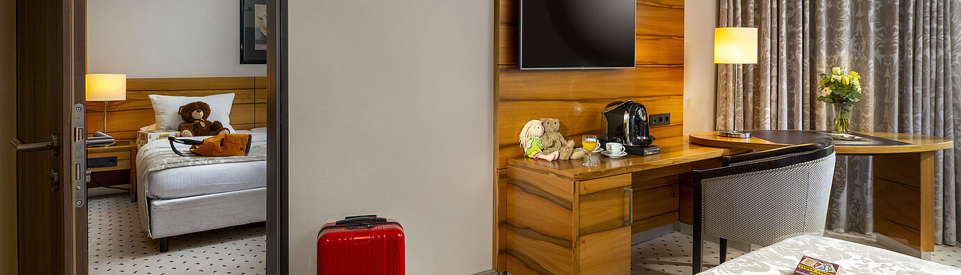 Camera di famiglia Superior Camera familiare al Maritim Hotel Bad Homburg con stanza separata per bambini, valigia rossa e orsacchiotto.