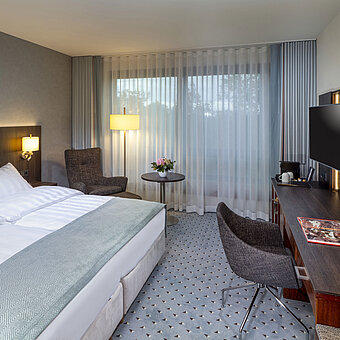Moderna habitación doble Superior del Hotel Maritim de Bremen con zona de estar, escritorio y una amplia y luminosa ventana.