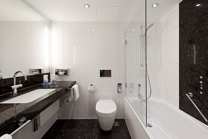 Modern bathroom at Maritim Hotel Darmstadt with elegant bathtub, dark granite countertop, and bright wall design.