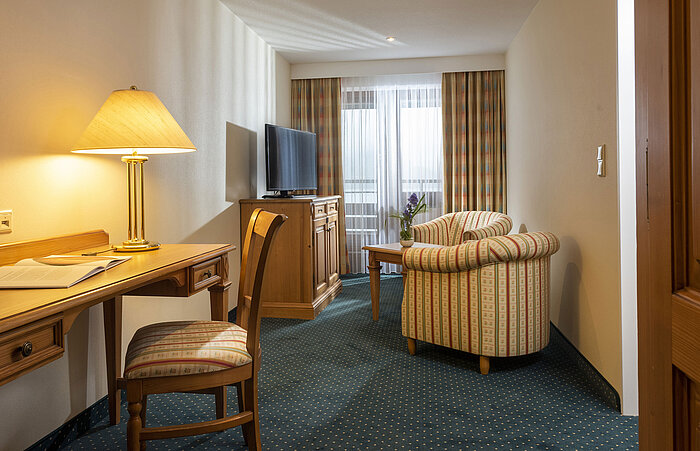 Living area with TV, desk and comfortable armchairs at Maritim Hotel Titisee