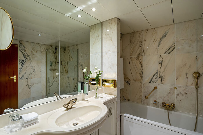Bagno moderno al Maritim Hotel Hannover con vasca, doccia in vetro e pareti in marmo.