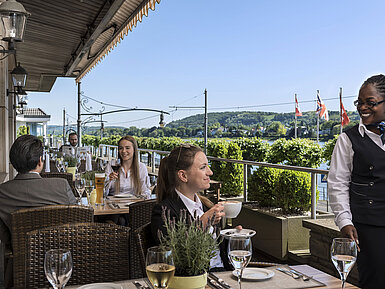 Des clients profitent d’un café et de vin sur la terrasse du Maritim Hotel Königswinter avec vue pittoresque sur le Rhin.