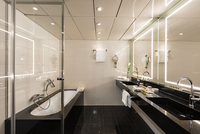 Ampio bagno suite con vasca moderna, doppi lavandini e illuminazione elegante al Maritim Hotel Bonn.
