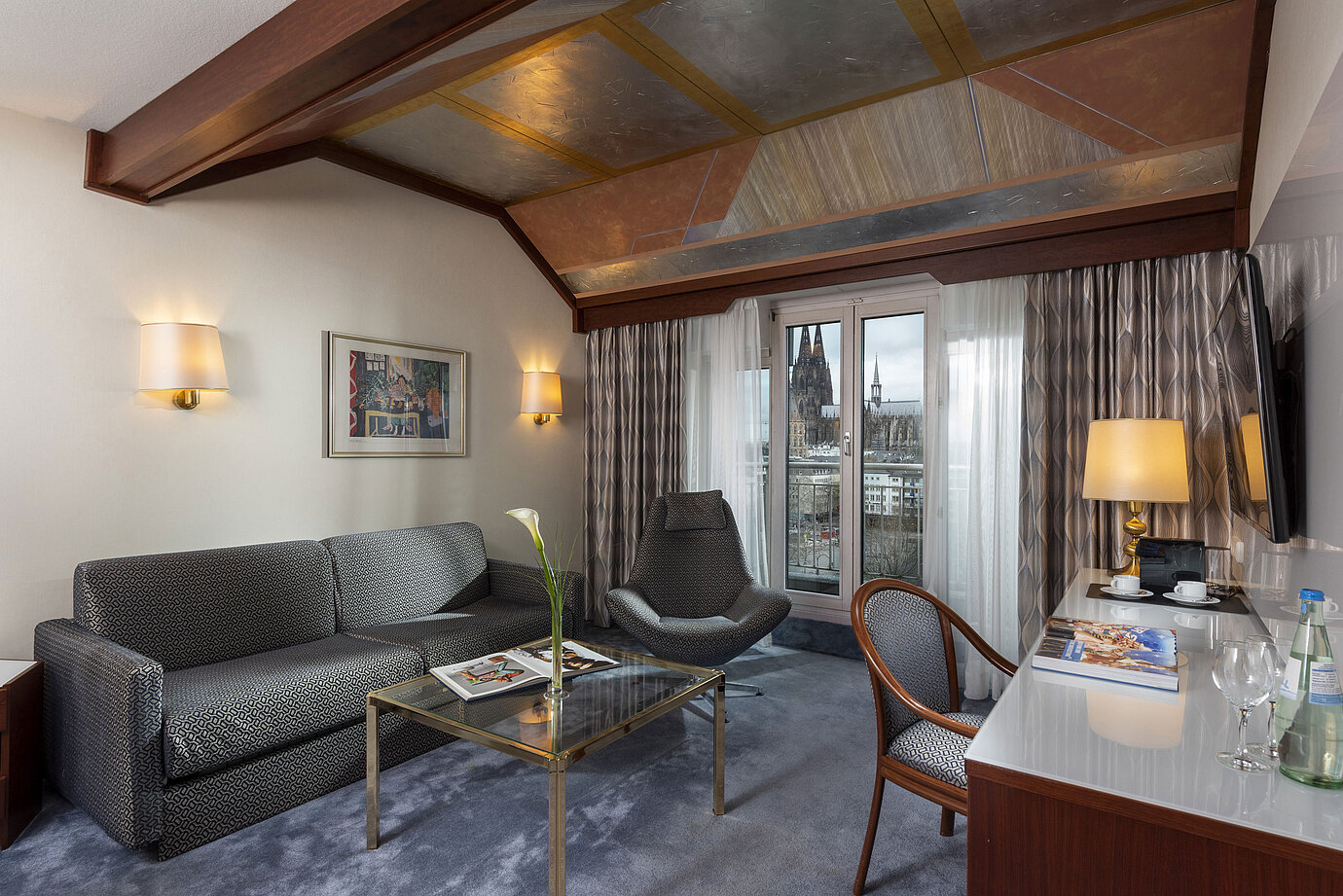 Junior Suite al Maritim Hotel Colonia con vista sulla Cattedrale di Colonia, elegante divano,poltrona e scrivania con letture