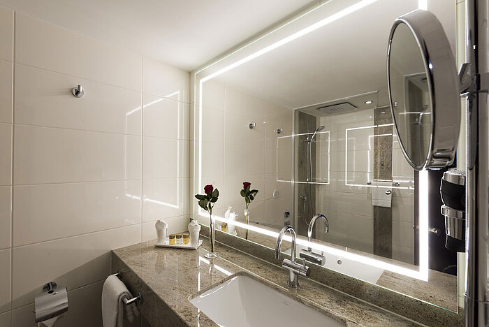Bagno moderno del Maritim Hotel Würzburg con grande specchio illuminato e piano in granito.