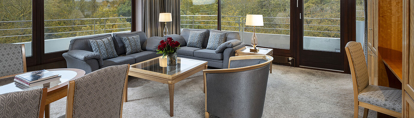 Sala de estar de la Grand Suite en el Maritim Hotel Kiel con grandes ventanas, decoración elegante y vistas a la naturaleza.