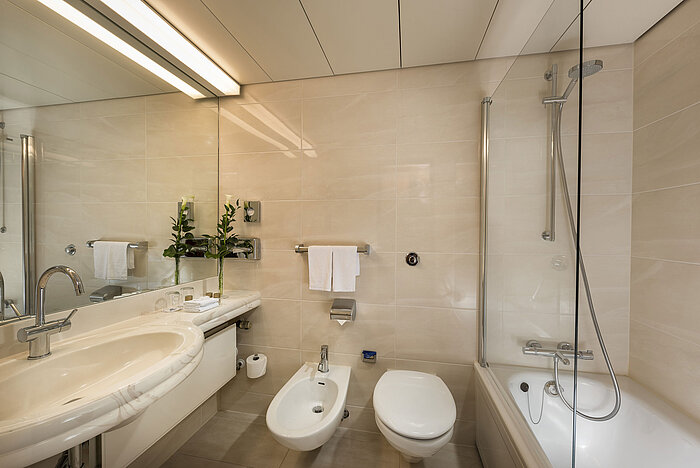 Bagno moderno con vasca, doccia, bidet e grande specchio al Maritim Hotel Hannover.