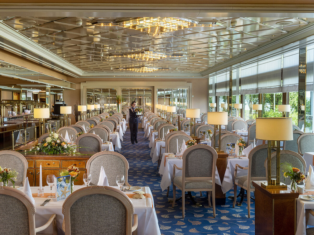 Grand restaurant élégant avec de longues tables dressées, des lustres et des arrangements floraux pour un repas raffiné.