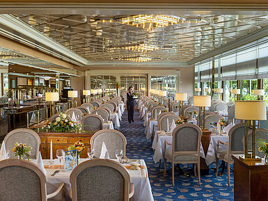 Grande ristorante elegante con lunghe tavole apparecchiate, lampadari e composizioni floreali per cene raffinate.