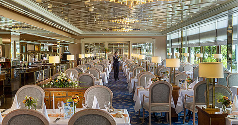 Grand restaurant élégant avec de longues tables dressées, des lustres et des arrangements floraux pour un repas raffiné.