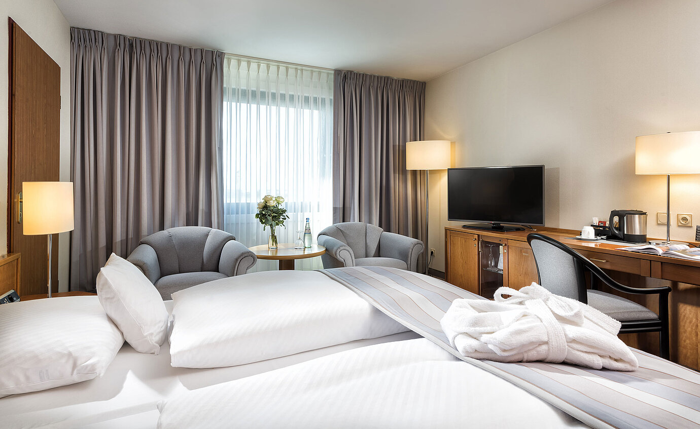 Camera doppia superior con arredi eleganti, accogliente area salotto, bottiglie d'acqua e accappatoio sul letto.
